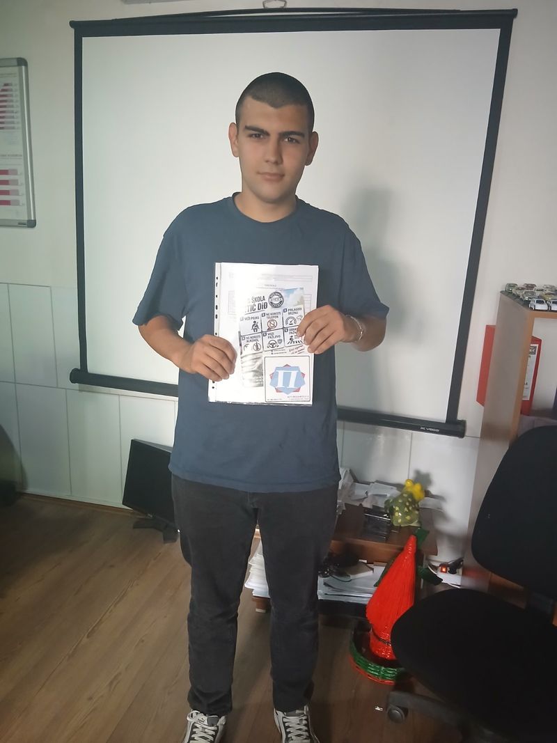 Polaznik auto škole Mitić D i Đ ispred platna u učionici sa plakatom škole u rukama